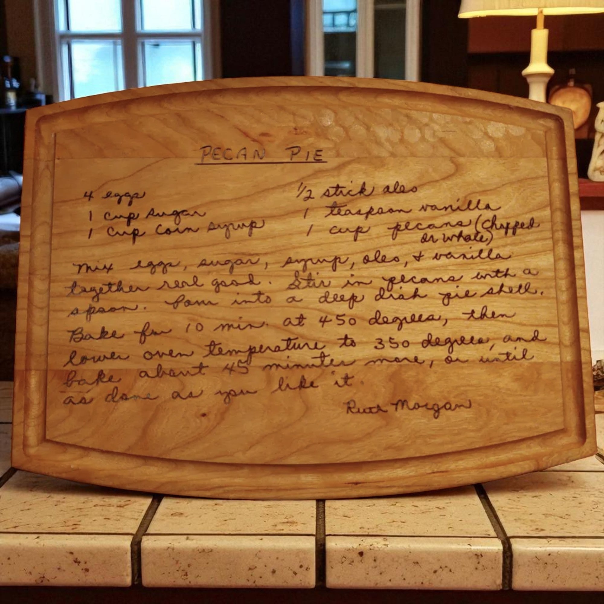 Wooden cutting board with engraved pecan pie recipe on a kitchen counter.