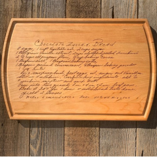 Wooden cutting board with engraved chocolate zucchini bread recipe on a wooden surface