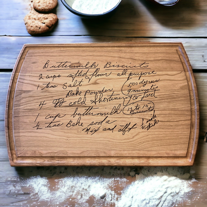 Cherry hardwood cutting board with engraved handwritten buttermilk biscuits recipe on a wooden surface.