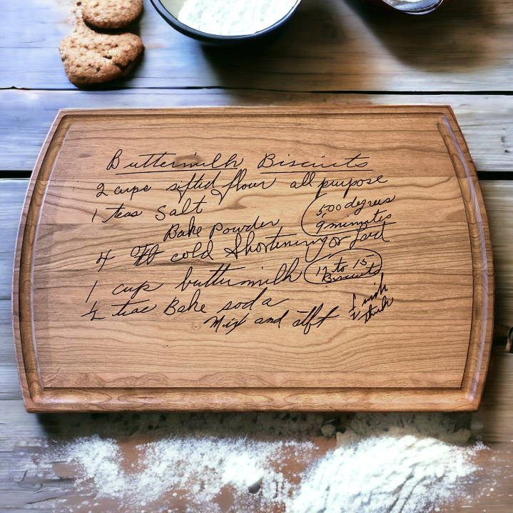 Cherry hardwood cutting board with engraved handwritten buttermilk biscuits recipe on a wooden surface.