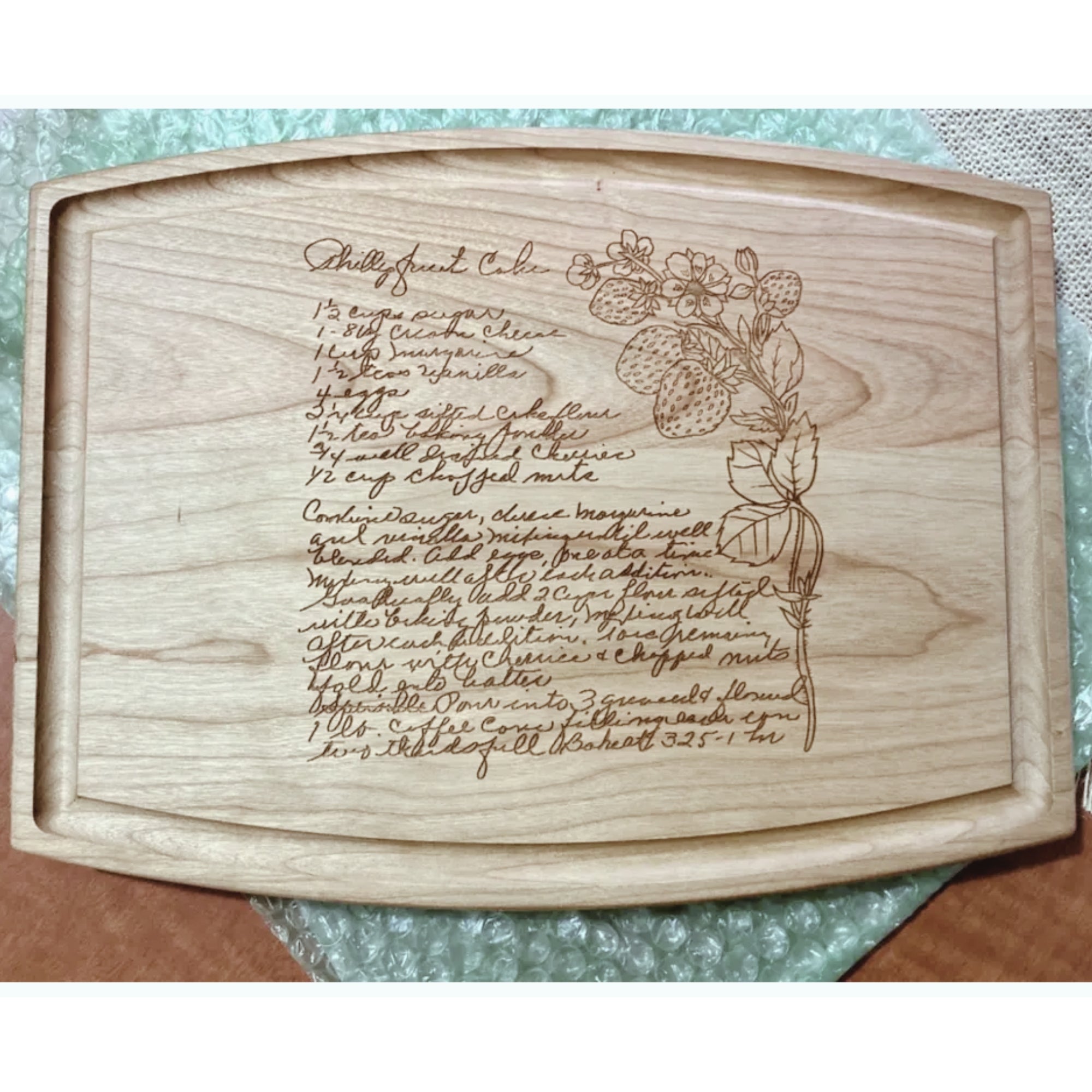 Wooden cutting board with engraved floral design and handwriting on a textured surface